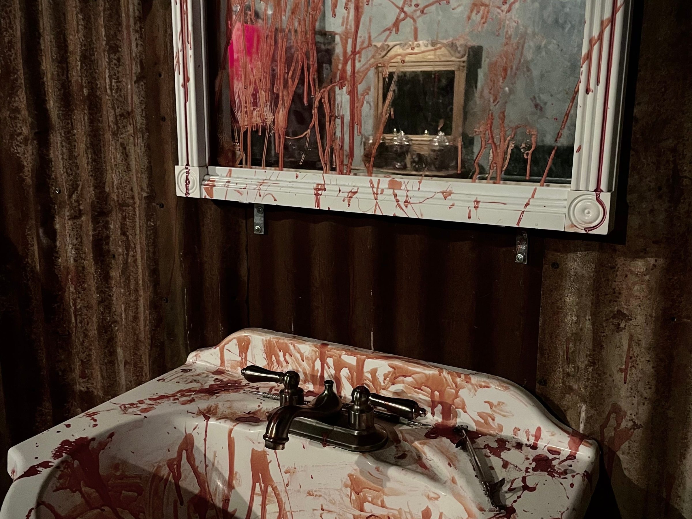 Sink and mirror splattered with red liquid resembling blood, creating a horror-themed scene.