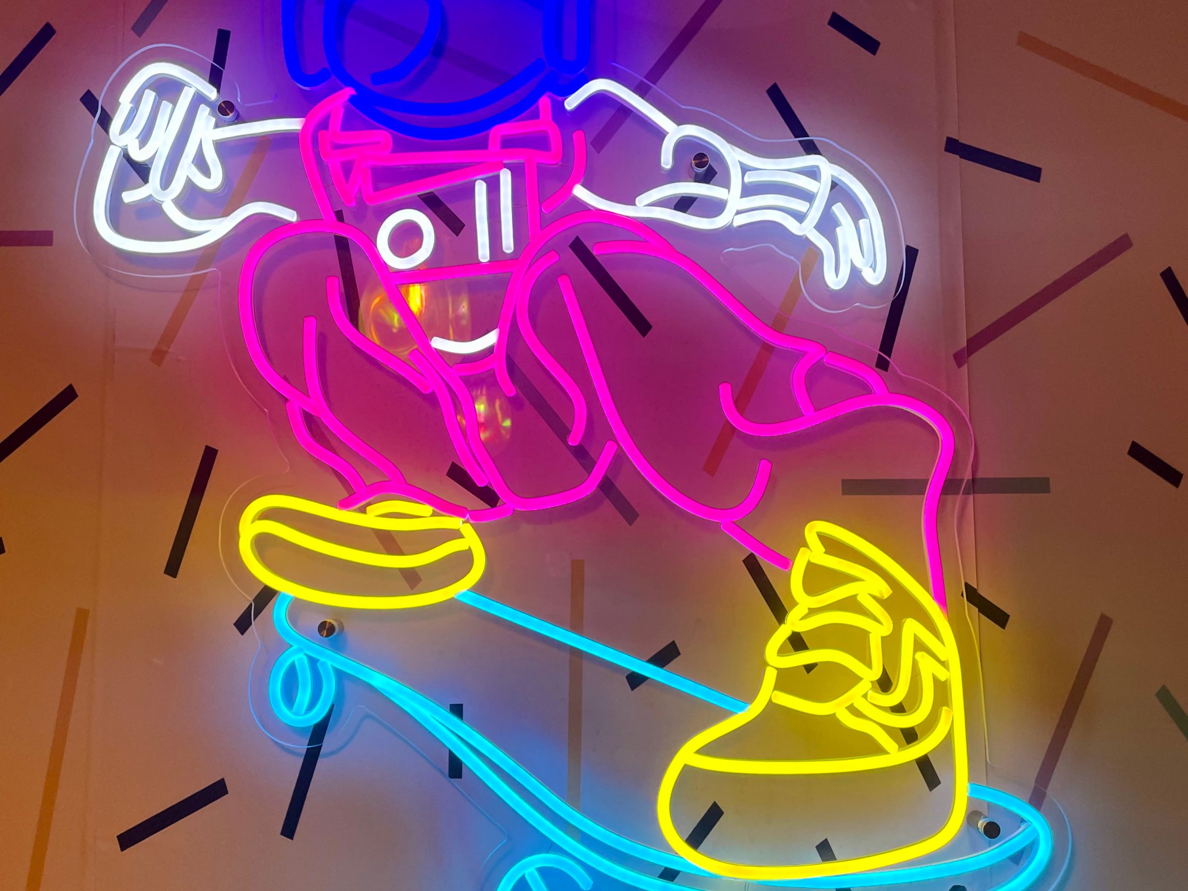 Neon lights of an astronaut skateboarding with a colorful geometric background.