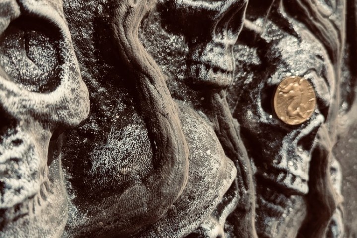 Close-up of carved skulls on a dark surface with a gold coin.