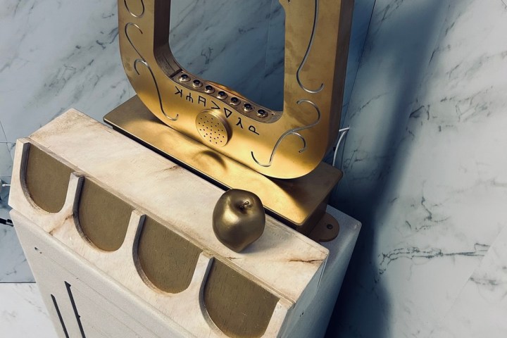 Artistic gold sculpture on marble pedestal with apple accent, in a tiled room.