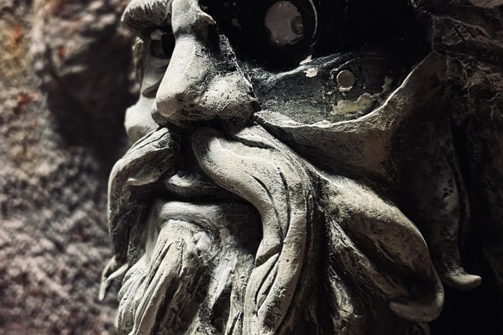 Close-up of a weathered stone statue with a detailed beard and hollow eyes.