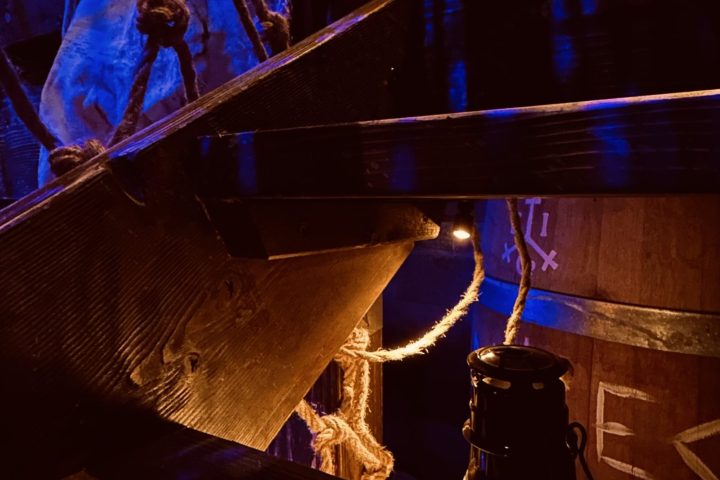 Dimly lit wooden stairs with ropes and a lantern, under blue lighting.