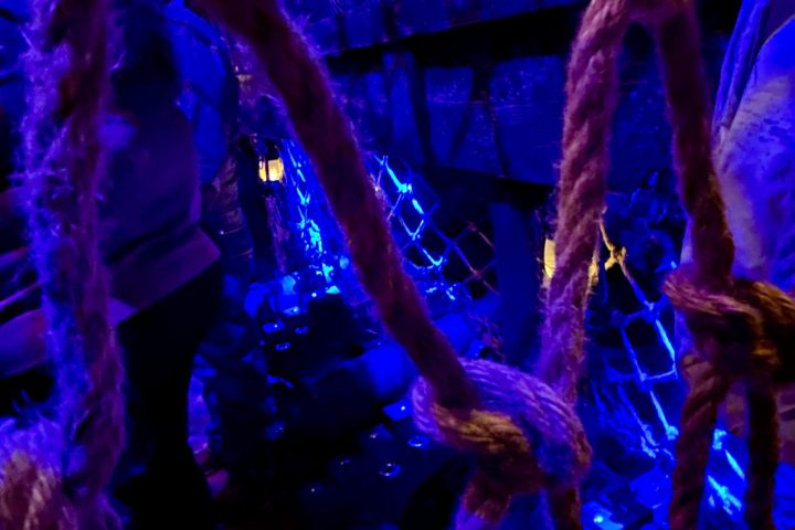 Rope net under blue light with a dark background of chains and crates.