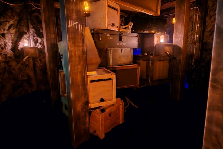 Dimly lit interior with stacked wooden crates and glowing lanterns in a rustic setting.