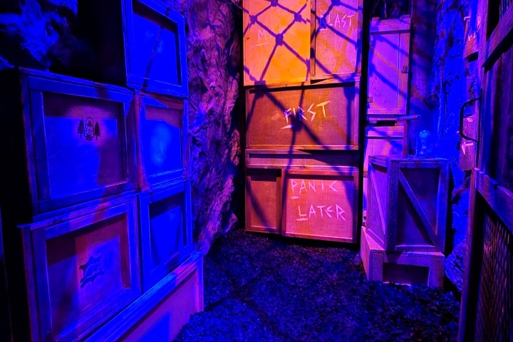 Dimly lit escape room with stacked crates under purple and orange lighting.