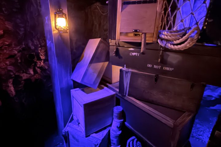 Room with crates, ropes, and a lantern lit in blue light.