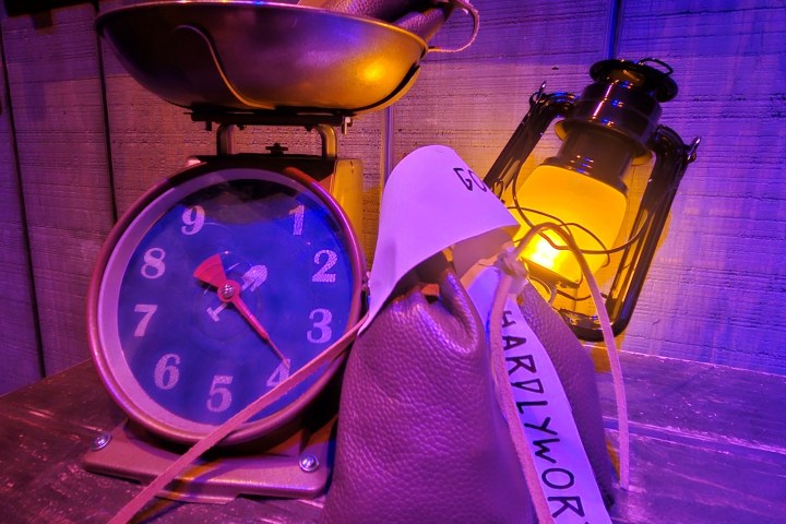 Vintage scale with bags, lit lantern in purple ambiance on wooden surface.