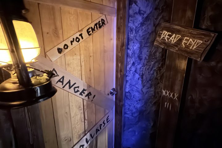 Wooden signs with warnings and lantern light on a dark wall.