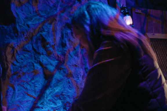 Person adjusts a small lamp in a dimly lit, net-covered room.