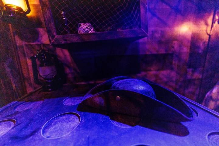 Dimly lit room with a tricorn hat on a table and lantern in the background.