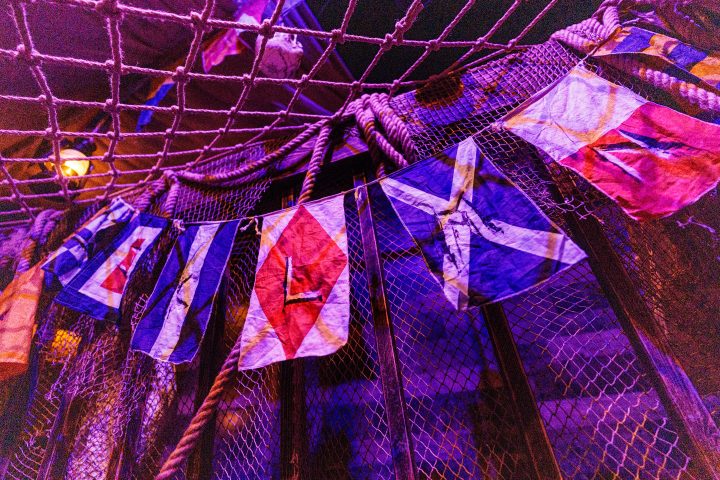 Colorful nautical flags hanging below a net under purple lighting.
