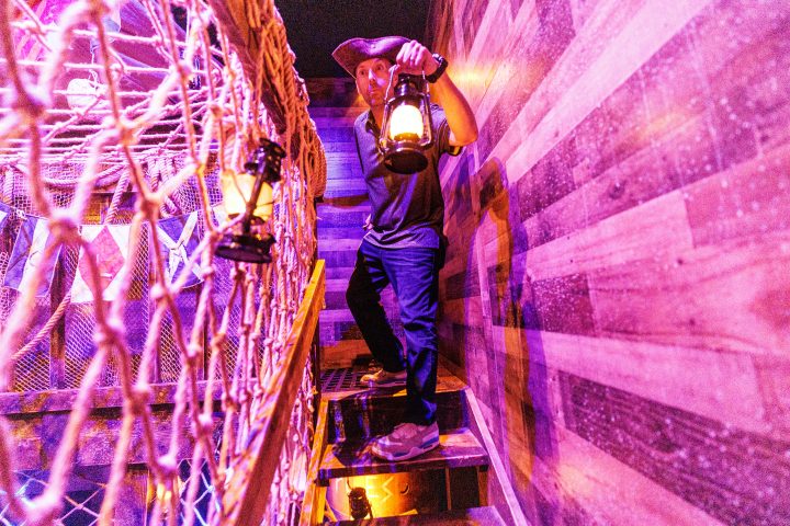 Person in pirate attire holds lantern on a wooden staircase.