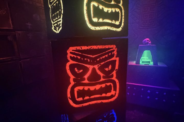 Colorful glowing totem faces in a dimly lit room with intricate wall patterns.