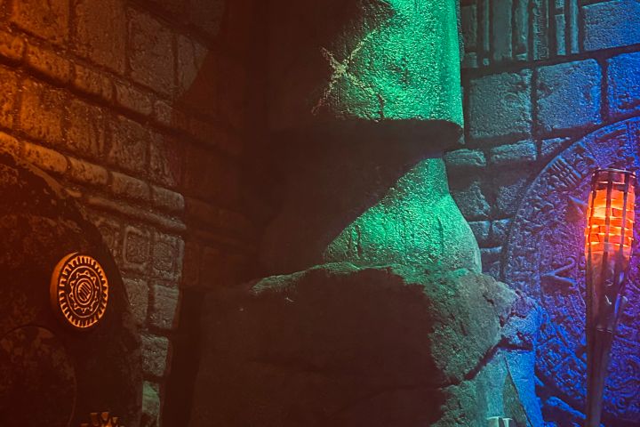 Moai statue in dimly lit room with colorful lights and stone decorations.