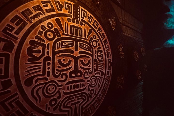 Illuminated ancient Mayan-style circular stone carving with intricate patterns.