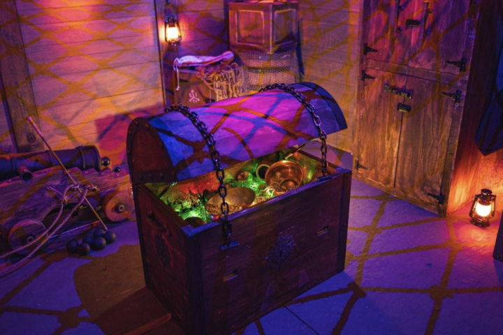 Open treasure chest with glowing jewel-toned lights and golden items in a dimly lit room.