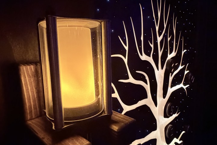 A glowing wall light next to a painted white tree on a dark background.