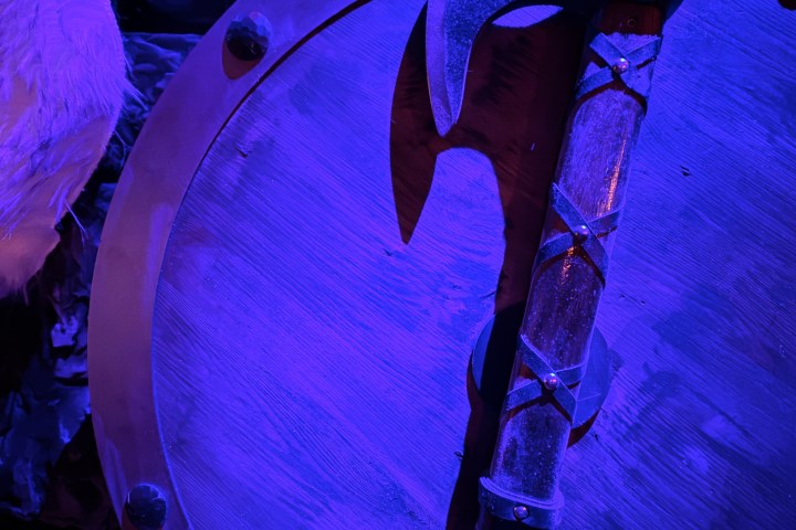 Axe with ornate handle on a shield, lit in purple light.