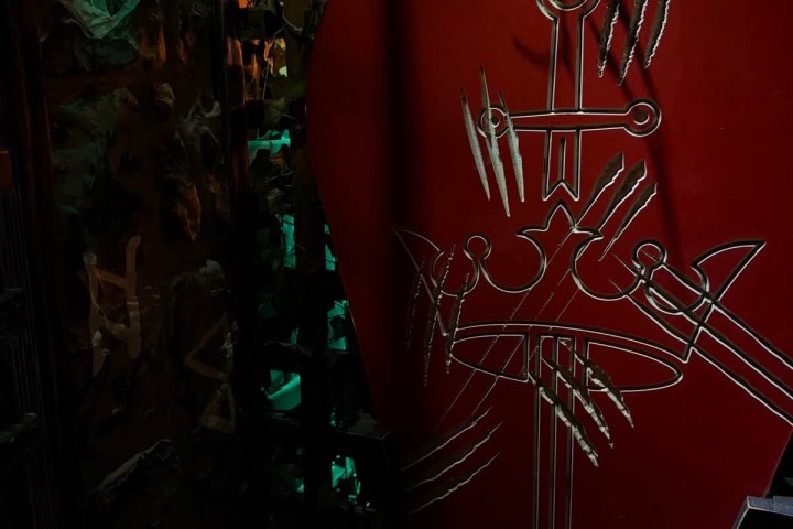 Red shield with swords and claw marks design against a dark, leafy background.
