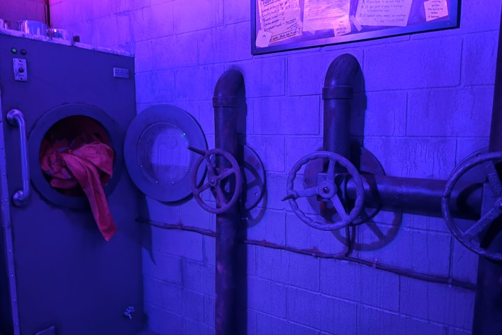 Industrial pipes and machinery in a dimly lit room with purple lighting.