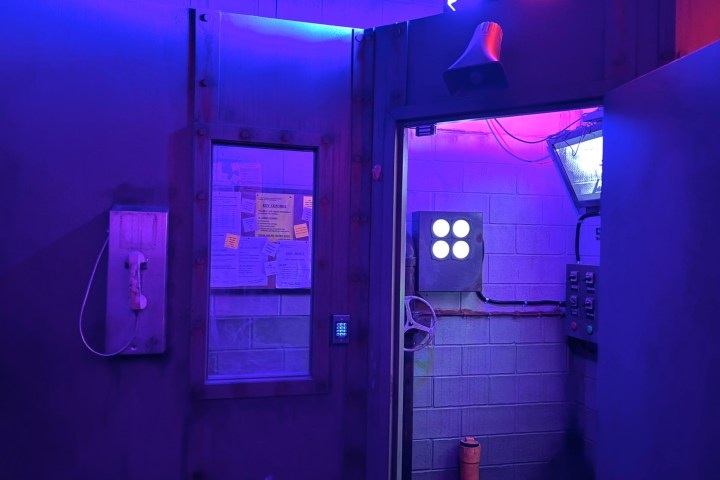 Dimly lit room with blue and purple lights, old phone, control panel, and bulletin board.