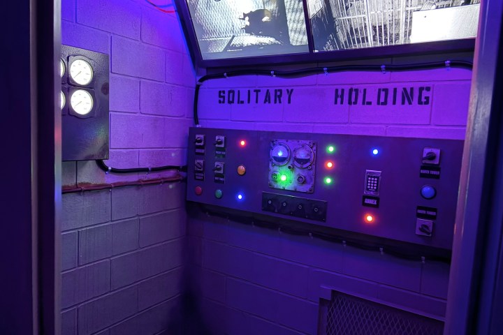 Control panel with lights in a room labeled 'Solitary Holding' under purple lighting.