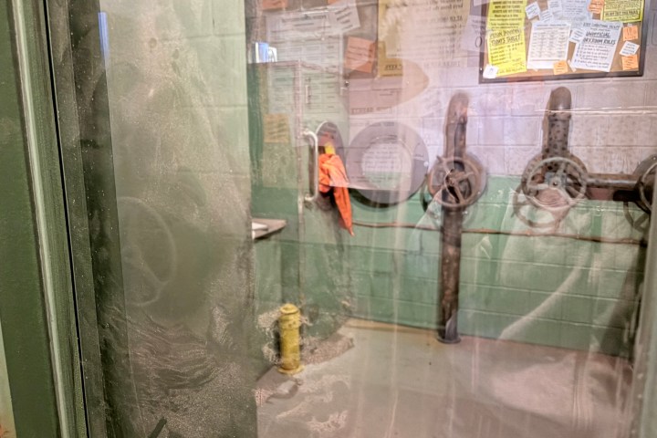 Dusty glass door into a cluttered room with wall posters and orange cloth.