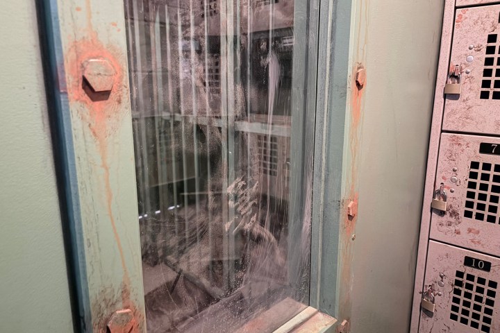Dusty equipment with glass panel and rusted metal bolts in an industrial setting.