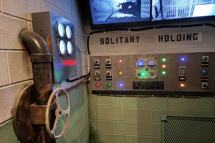Industrial control panel with gauges and monitors labeled 'Solitary Holding' in a dimly lit room.
