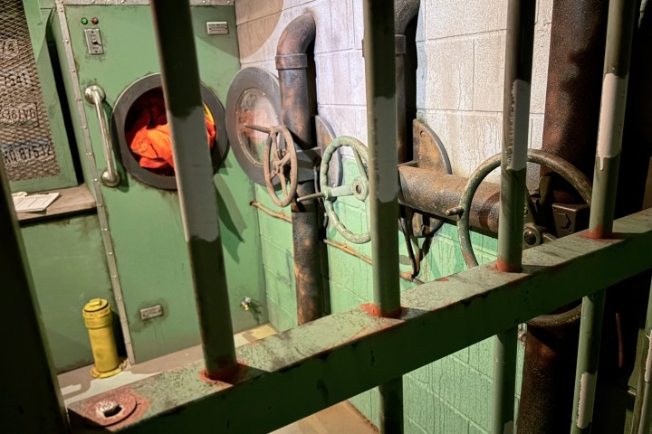 Industrial room with pipes, valves, and a green machine behind bars.