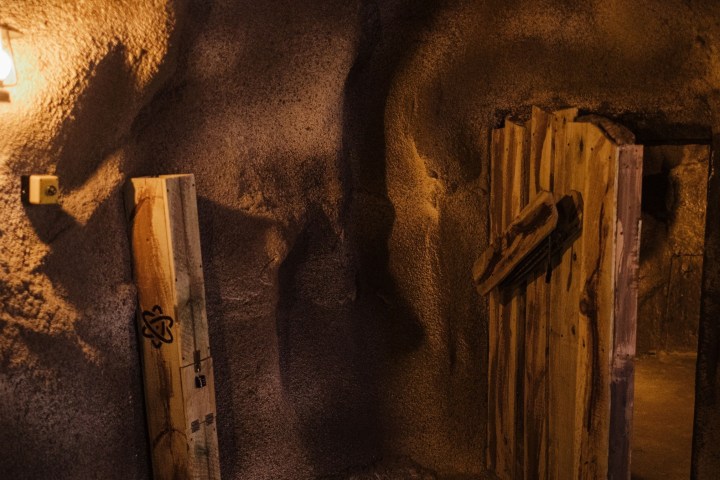 Rustic wooden door in a dimly lit cave-like room with a lantern.
