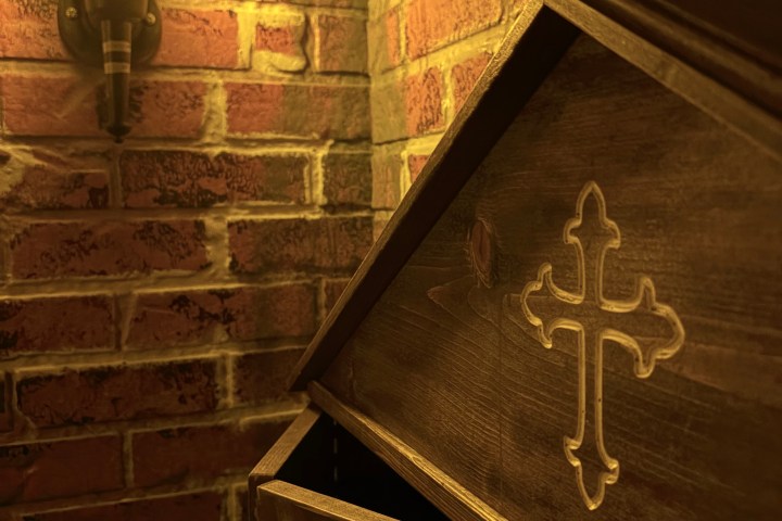 Wooden box with a cross on brick wall, lit by lantern.