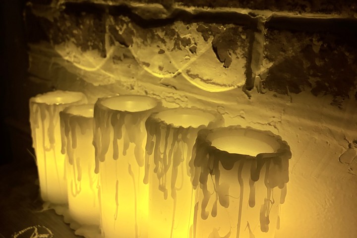 Four candles with dripping wax against a textured brick wall.