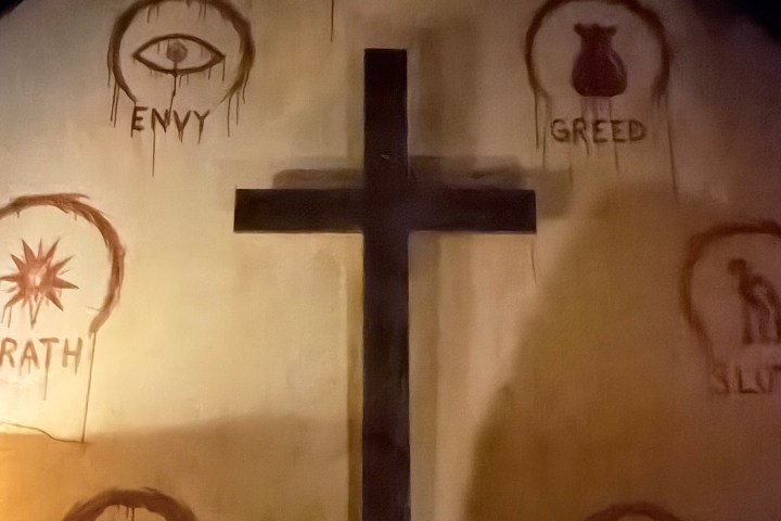 Wall with a cross and symbols of the seven deadly sins painted around it.